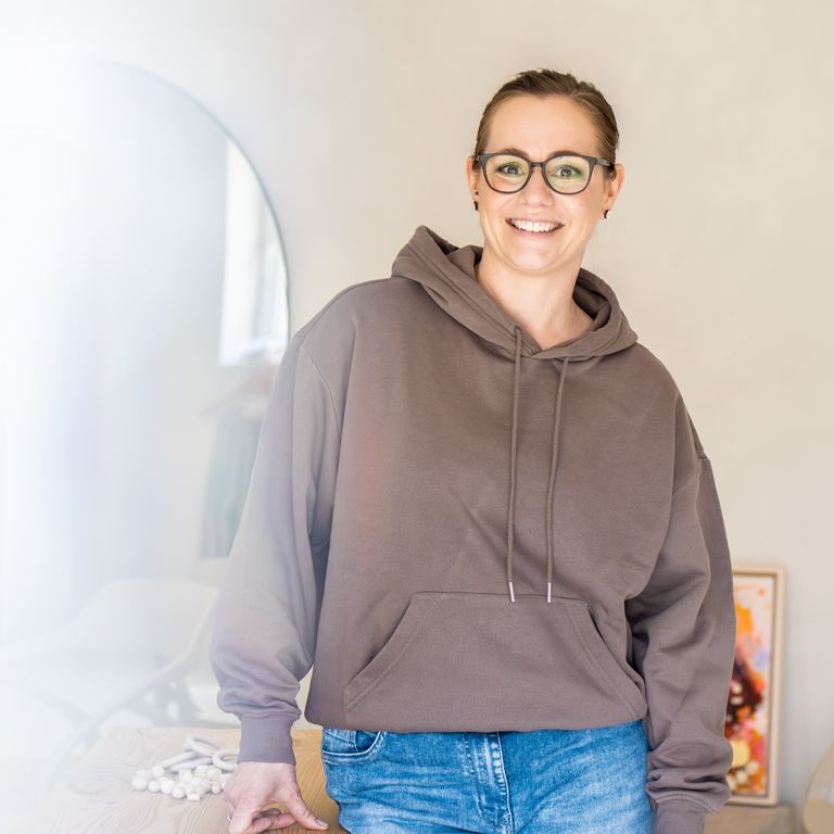 Porträt der Inhaberin von ‚Per Hand‘, freundlich lächelnd, vor einem Tisch.