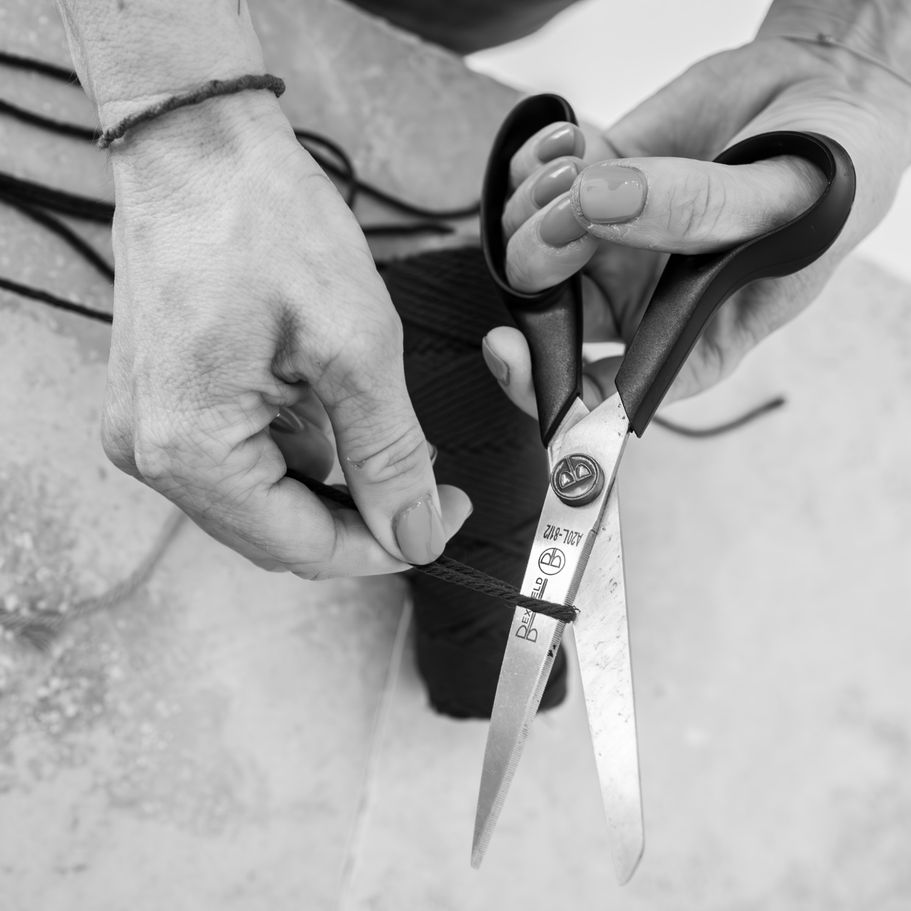 Hände halten eine Schere und schneiden Makrameegarn für handgemachte Dekoration.