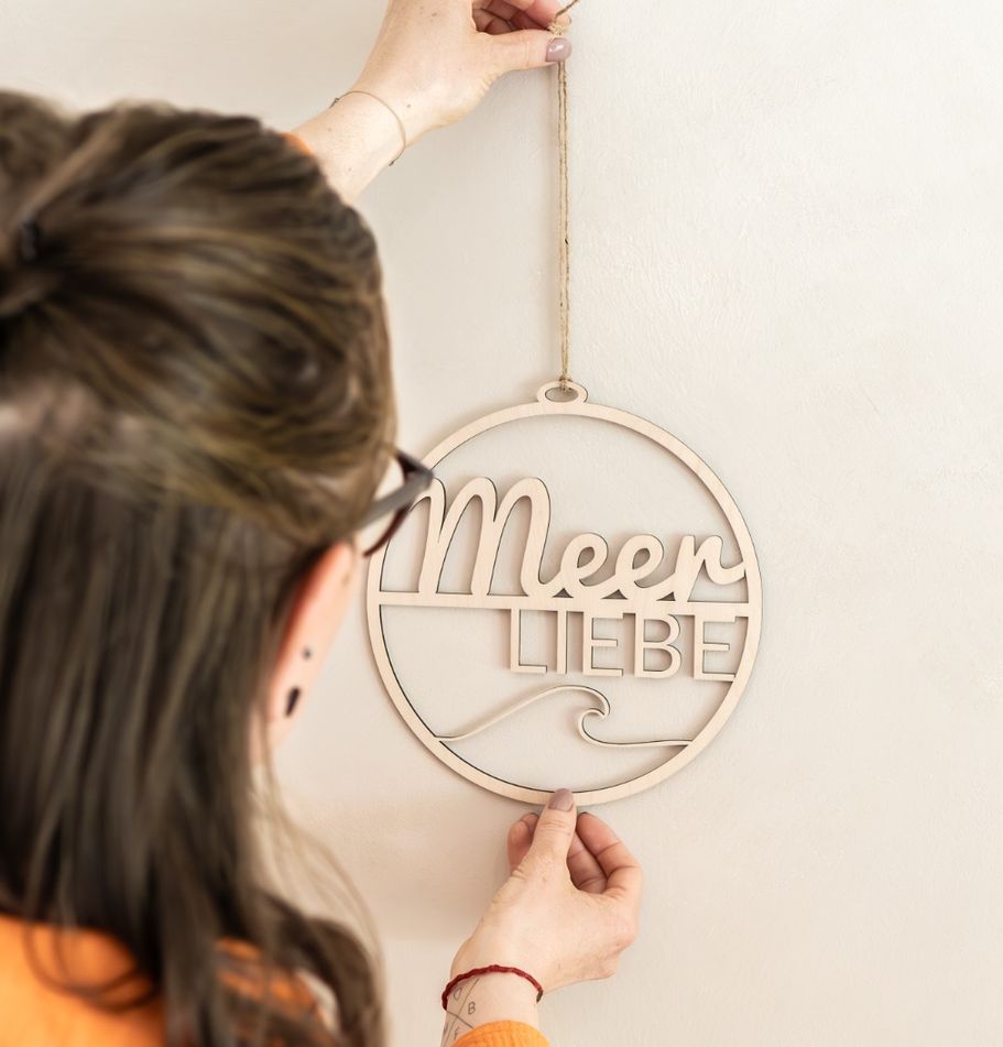 Inhaberin hängt Holzkranz mit „Meerliebe“-Schriftzug an die Wand.